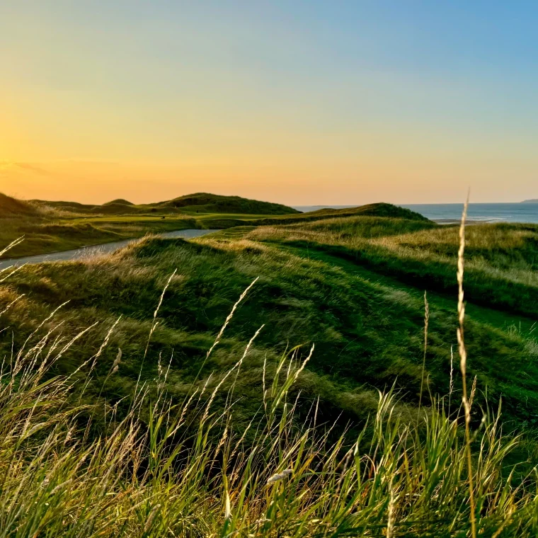 Sunset over grassy hills and ocean.
